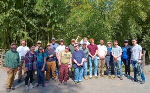 Group photo of about 20 workplace volunteers standing in front of a bamboo grove. They’re smiling, with dirt on their clothes and faces, looking tired but happy after a day of outdoor work.