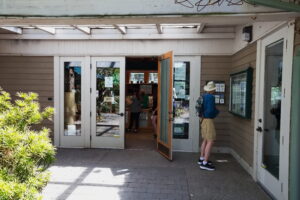 Glass front doors of the Visitor Center with a person standing outside at a brochure rack taking a trail map.