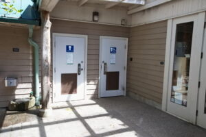 A picture in the Visitor Center courtyard of the 2 all gender bathroom doors and drinking fountains to the left of the doors.