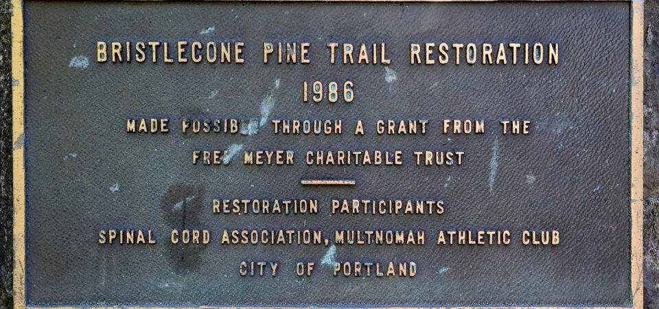 A metal plaque that reads: "Bristlecone Pine Trail Restoration 1986. Made possible by a grant from Fred Meyer Memorial Trust. Restoration participants: Spinal Cord Association, Multnomah Athletic Club, City of Portland."